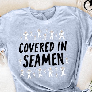May include: A light blue t-shirt with a white sailor graphic and the text "COVERED IN SEAMEN" in black.