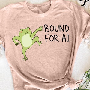 May include: A light pink t-shirt with a green frog graphic and the text "BOUND FOR AI".