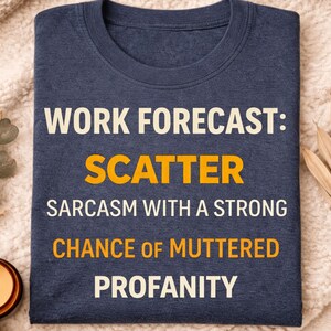 May include: Navy blue t-shirt with the text "WORK FORECAST: SCATTER SARCASTIC WITH A STRONG CHANCE OF MUTTERED PROFANITY" in white and orange lettering. The shirt is displayed on a cream-colored blanket.