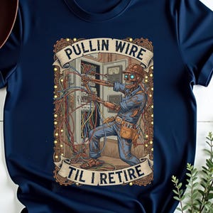 May include: Navy blue t-shirt featuring a detailed graphic of a skeleton electrician working on wires. The image includes the text "PULLIN WIRE TIL I RETIRE" in a banner design. The shirt has short sleeves and a crew neck.