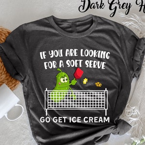 Könnte beinhalten: Dunkelgraues T-Shirt mit einem weißen Aufdruck eines Gurkens, der Tischtennis mit einem Keks spielt. Der Text auf dem Shirt lautet "Wenn du nach einem Soft-Serve suchst, hol dir Eis."