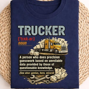 Peut inclure: T-shirt bleu marine avec le mot "TRUCKER" en police vieillie. Le t-shirt présente un dessin de semi-remorque jaune et un texte définissant un camionneur. Le t-shirt est plié sur un tapis tissé.