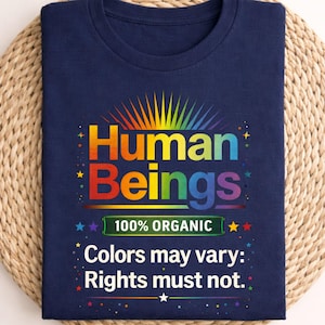 May include: Navy blue t-shirt with the words "Human Beings" in rainbow colors, with a sunburst design above. The shirt also says "100% Organic" and "Colors may vary: Rights must not."