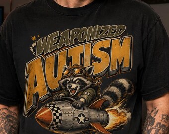 Peut inclure: Un t-shirt noir avec une illustration d'un raton laveur portant des lunettes d'aviateur et une veste, chevauchant une fusée. Le texte "WEAPONIZED AUTISM" est imprimé en grandes lettres jaunes usées au-dessus du dessin du raton laveur.