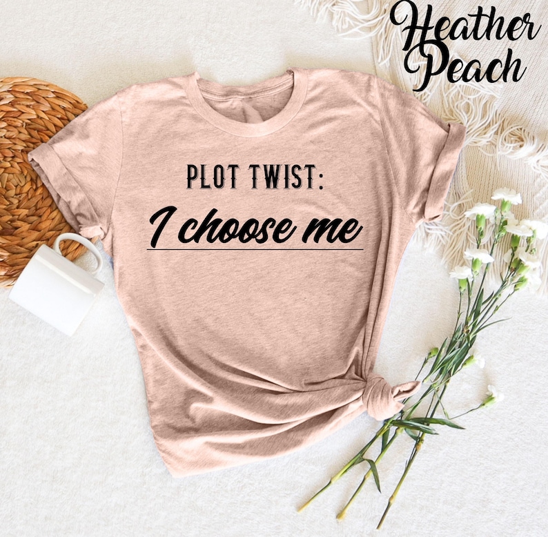 May include: A heather peach colored t-shirt with the text "PLOT TWIST: I choose me" printed in black.