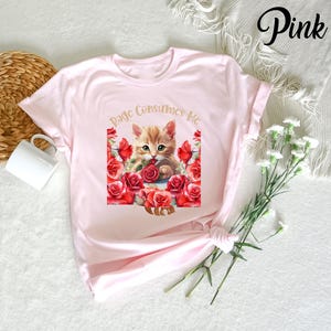 May include: A light pink t-shirt featuring a graphic of a ginger kitten surrounded by red roses. The text "Page Consumes Me" is arched above the kitten. The word "Pink" is written in cursive in the upper right corner.