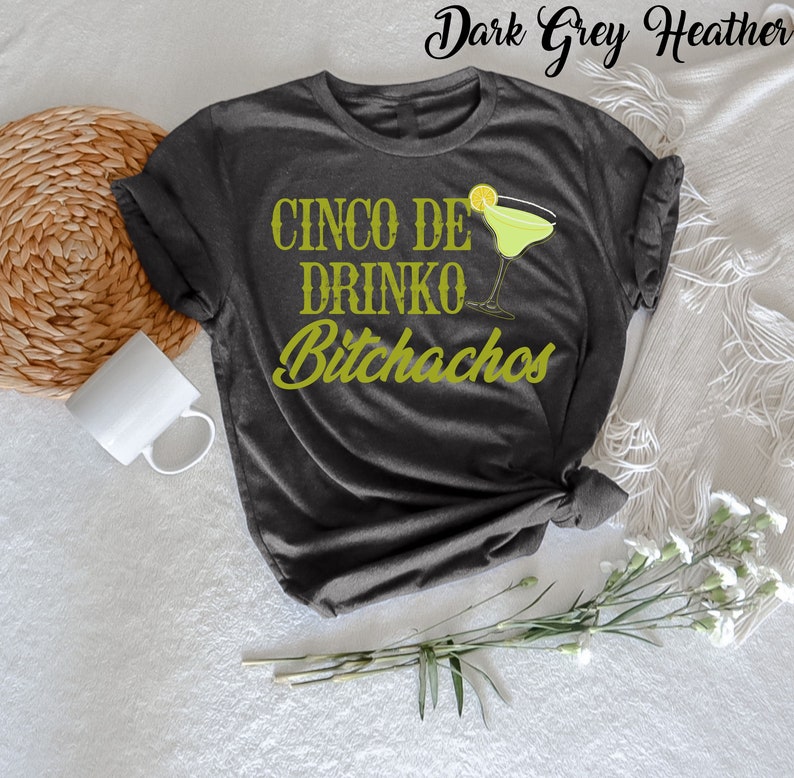 May include: Dark grey heather t-shirt with the text "Cinco De Drinko Bitchachos" in green lettering. A green margarita glass with a lime wedge is next to the text.