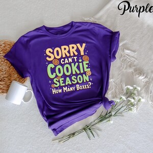 May include: Purple t-shirt with the text "Sorry can't cookie season. How many boxes?" in green and yellow text with cookie images.