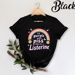 May include: Black t-shirt with a rainbow and the text "I'll gargle your piss like it's Listerine" in pink.