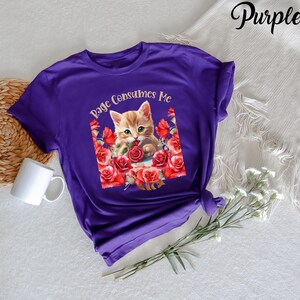 May include: A purple t-shirt featuring a graphic of a ginger kitten surrounded by red roses. The text "Rage Consumes Me" is arched above the kitten. The word "Purple" is written in cursive in the upper right corner.