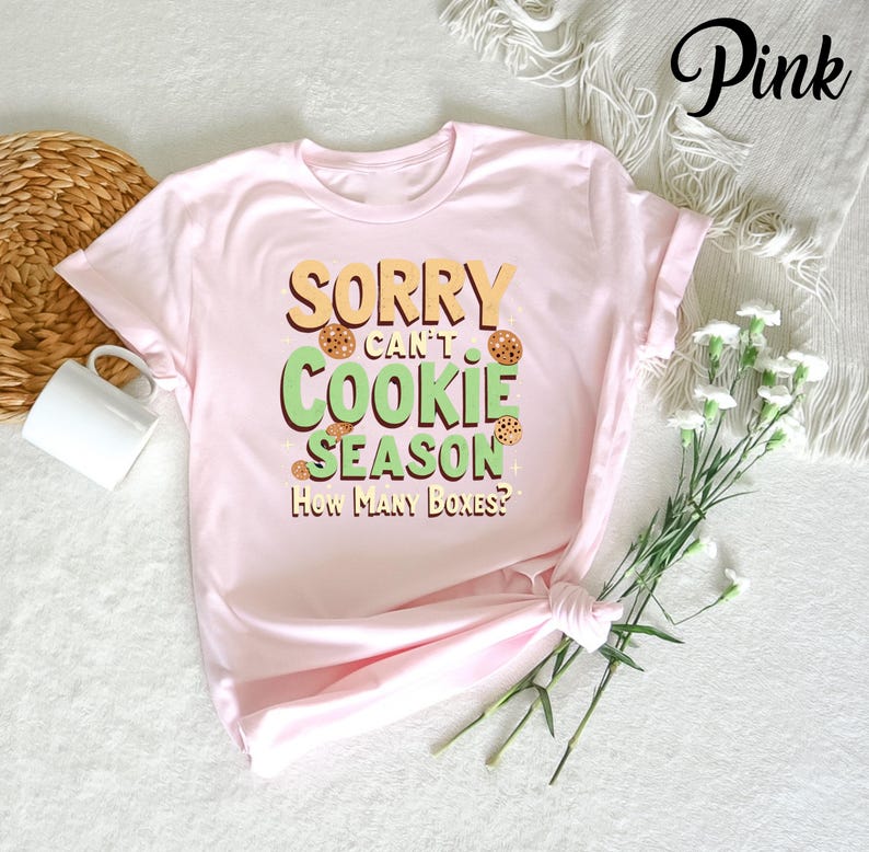 May include: Pink t-shirt with the text "Sorry can't cookie season. How many boxes?" in green and yellow letters. The text is surrounded by images of chocolate chip cookies.