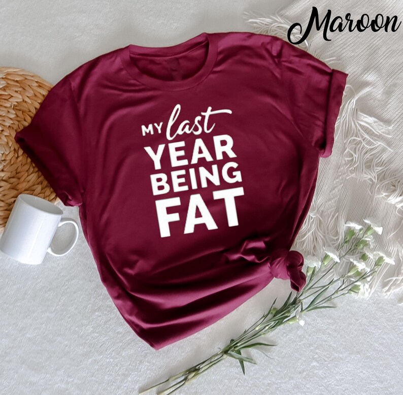 May include: A maroon t-shirt with the text "My last year being fat" in white.
