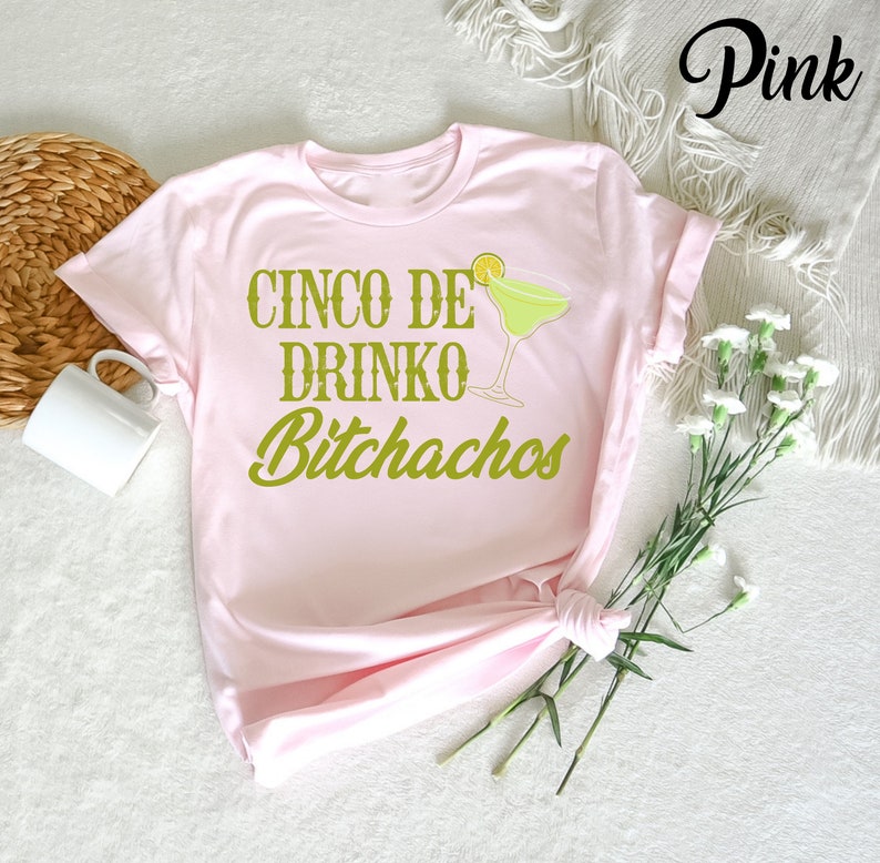 May include: Pink t-shirt with the text "Cinco de Drinko Bitchachos" in green lettering and a green margarita glass with a lime wedge.