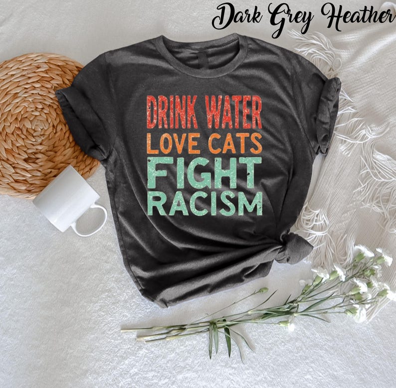 May include: Dark grey heather t-shirt with the text "Drink Water Love Cats Fight Racism" in a vintage style font.