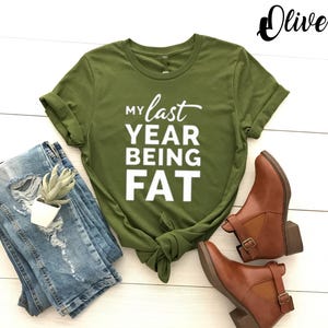 May include: A green t-shirt with the text "My last year being fat" in white letters.