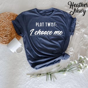 May include: A heather navy blue t-shirt with the text "PLOT TWIST: I choose me" printed in white.