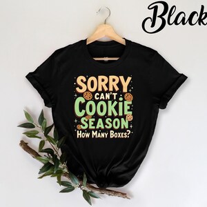 May include: Black t-shirt with a green and white graphic that says "Sorry can't cookie season. How many boxes?" with cookie images.