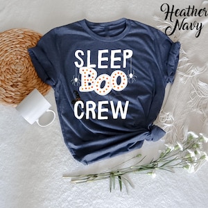May include: A heather navy blue t-shirt with the text "SLEEP BOO CREW" in white. The word "BOO" is decorated with orange and yellow polka dots and surrounded by black spider webs.