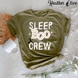 May include: A green t-shirt with the text "SLEEP BOO CREW" in white letters. The word "BOO" is decorated with orange and white polka dots and a spider web.