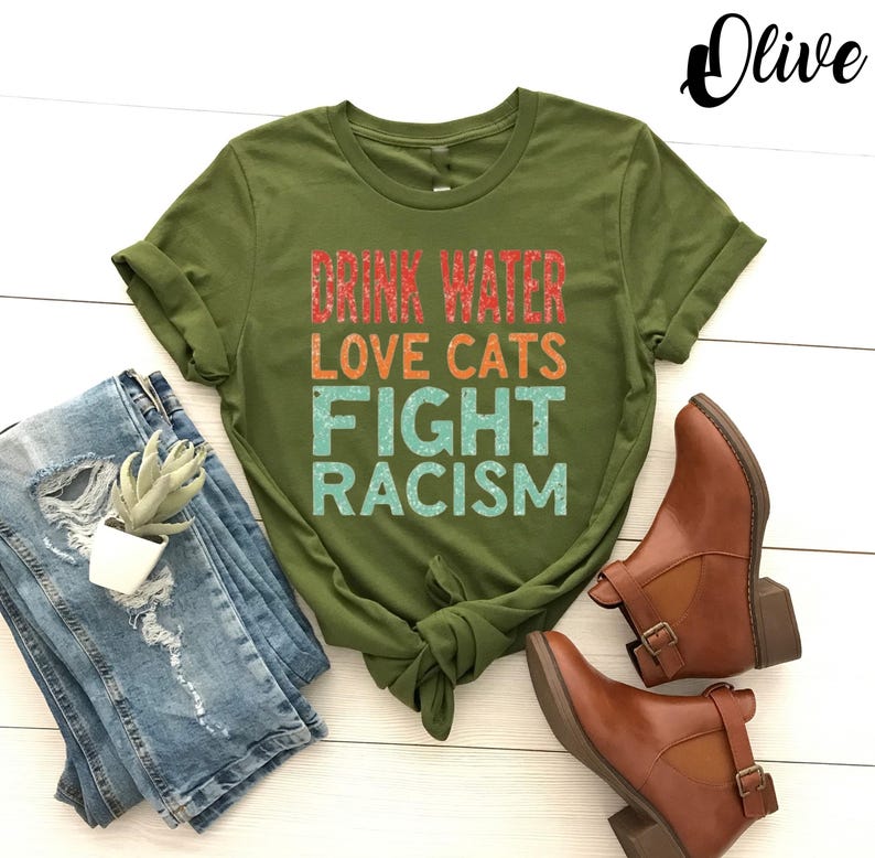 May include: Olive green t-shirt with the text "Drink Water Love Cats Fight Racism" in a rainbow color scheme.