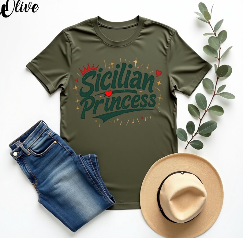 以下が含まれることがあります： 緑色のTシャツに「シチリアのプリンセス」という文字が緑色、赤色、金色のフォントで書かれています。文字の周りは小さな金色の星と赤いハートで囲まれています。