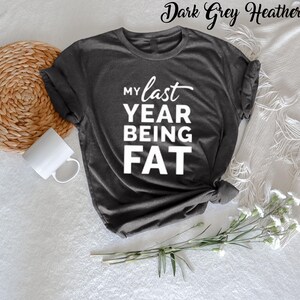 May include: Dark grey heather t-shirt with the text "My last year being fat" in white.
