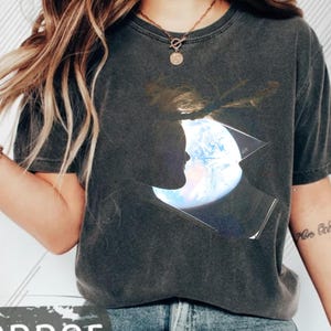 May include: Dark gray t-shirt with a graphic of a silhouette of a person's face with the Earth inside a geometric shape. The word "Pepper" is at the bottom left of the shirt.