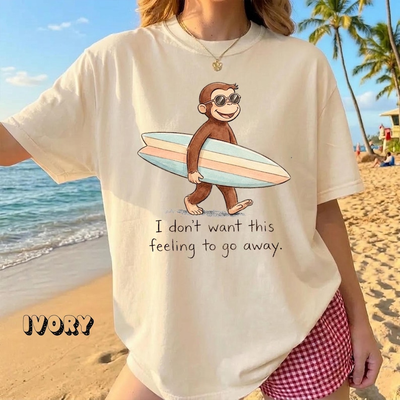 May include: Ivory-colored t-shirt featuring a cartoon monkey wearing sunglasses and carrying a surfboard. The shirt has the text "I don't want this feeling to go away." The word "IVORY" is printed at the bottom left.