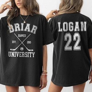 Może przedstawiać: Czarny t-shirt z napisem "BRIAR HAWKS UNIVERSITY", skrzyżowanymi kijami hokejowymi i "EST. 2015" z przodu. Tył koszulki zdobi napis "LOGAN 22" w kontrastowym kolorze.
