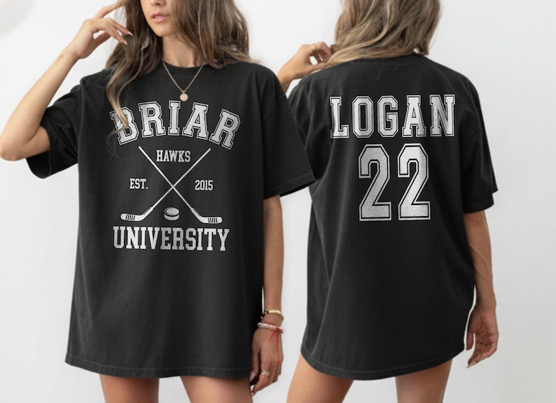 Może przedstawiać: Czarny t-shirt z napisem "BRIAR HAWKS UNIVERSITY", skrzyżowanymi kijami hokejowymi i "EST. 2015" z przodu. Tył koszulki zdobi napis "LOGAN 22" w kontrastowym kolorze.