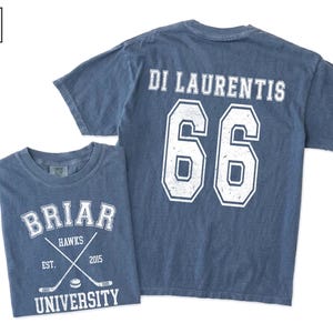 May include: A blue jean colored t-shirt featuring a white graphic on the front that reads BRIAR UNIVERSITY, HAWKS, EST. 2015 with crossed hockey sticks and a puck. The back displays the name DI LAURENTIS above the large white jersey number 66.
