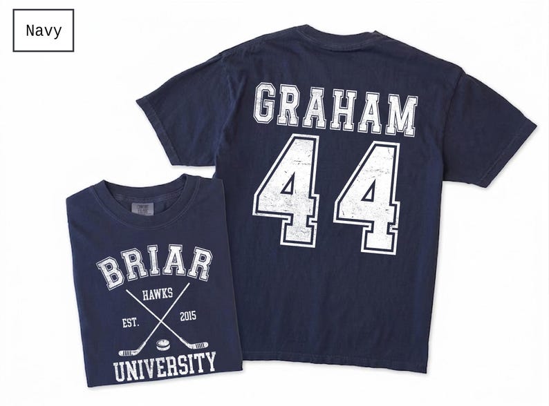 Puede incluir: Una camiseta azul marino de manga corta con un gr&aacute;fico blanco en la parte delantera que dice BRIAR UNIVERSITY HAWKS EST. 2015 con palos de hockey cruzados y un disco. La parte trasera muestra el nombre GRAHAM y el n&uacute;mero 44 en letras blancas.