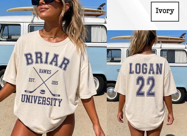 Może przedstawiać: Kremowa koszulka z napisem "BRIAR HAWKS UNIVERSITY" w kolorze granatowym, z skrzyżowanymi kijami hokejowymi i krążkiem. Z tyłu koszulki napis "LOGAN 22" w kolorze granatowym. Koszulka jest noszona przez osobę przed niebieskim vanem.
