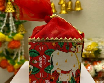 May include: A red fabric gift bag with gold trim, tied with a red ribbon. The bag is decorated with a printed design of a white cow and calf on a red background with green leaves and pink flowers.