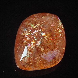 Op de afbeelding: Een gladde, oranje sunstone met een unieke, iriserende glans. De steen heeft een natuurlijke, vrije vorm en is perfect voor het maken van sieraden of kristallen genezing.