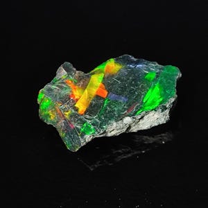 Könnte beinhalten: Ein roher, grüner und grauer Opal mit Schimmern in Gelb, Orange und Rot.