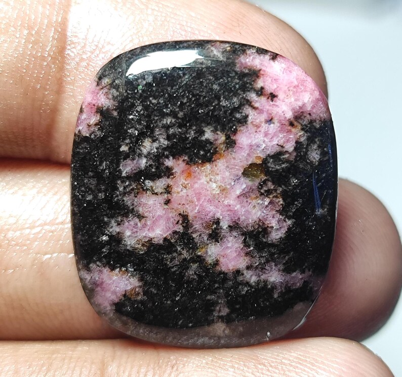 Puede incluir: Una piedra preciosa tallada en cabuj&oacute;n rosa y negra con un patr&oacute;n de remolino. La piedra preciosa est&aacute; pulida y tiene una superficie lisa.