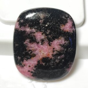 Puede incluir: Una piedra preciosa tallada en cabuj&oacute;n con un patr&oacute;n negro y rosa. La piedra tiene una superficie lisa y pulida y es un material natural y org&aacute;nico.