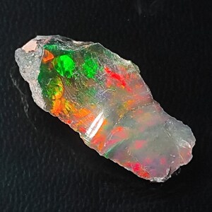May include: A rough, translucent, light gray opal with iridescent flashes of green, red, and orange.