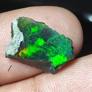 Könnte beinhalten: Ein rauer, dunkelgrüner und schwarzer Opal mit einem leuchtend grünen Schimmer. Der Opal ist ein Naturstein und hat eine raue, unregelmäßige Form.