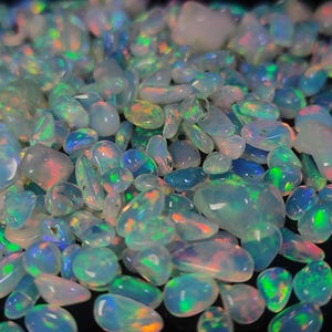 Könnte beinhalten: Eine Ansammlung von Opalen in verschiedenen Formen und Größen. Die Opale zeigen eine Reihe von Farben, darunter Blau, Grün, Orange und Weiß, mit schillernden Blitzen. Die Edelsteine sind glatt und poliert und reflektieren das Licht.