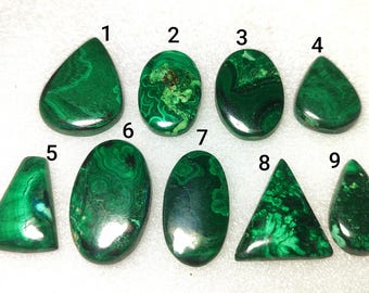 May include: Nine polished malachite gemstones in various shapes, including oval, teardrop, and triangular. The gemstones display a rich, swirling green pattern, with variations in color and texture. Each stone is numbered for identification.
