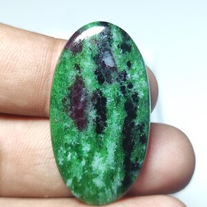 Op de afbeelding: Ovale groene, zwarte en roze edelsteen cabochon met een gepolijste afwerking.