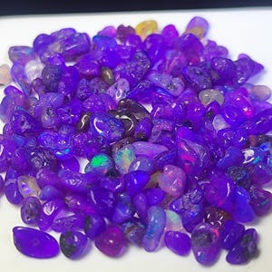 Könnte beinhalten: Ein Haufen polierter, violetter Opal-Edelsteine. Die Opale, in verschiedenen Größen und Formen, zeigen eine Reihe von Violetttönen. Einige Steine weisen schillernde Farbtupfer auf.