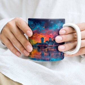 May include: A white ceramic mug with a colorful image of the London skyline at sunset. The image includes the London Eye, Big Ben, and other iconic landmarks. The mug is being held by a person's hands.