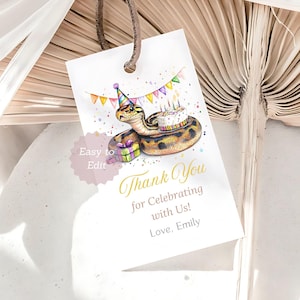 以下が含まれることがあります： パーティーハットとバースデーケーキをかぶったヘビの水彩イラストが描かれた白いギフトタグ。「Thank You for Celebrating with Us! Love, Emily.」と書かれています。
