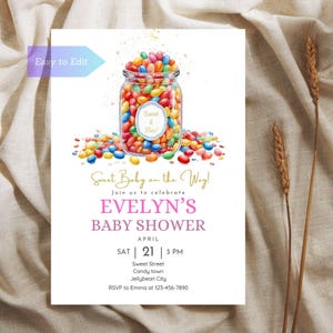 Può includere: Un invito a un baby shower con un'illustrazione ad acquerello di un barattolo di vetro pieno di caramelle gommose colorate. Il testo recita "Sweet Baby on the Way!" e "Evelyn's Baby Shower". La data e l'ora della doccia sono elencate come "April 21, 3 PM".