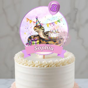Puede incluir: Un adorno para tarta con una serpiente de dibujos animados con un gorro de fiesta, una pequeña tarta y regalos. El adorno tiene una pancarta con el nombre "Sophia" y un globo morado con el número 8.