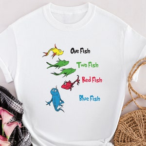 Puede incluir: Camiseta blanca con un gráfico de peces y el texto "One Fish, Two Fish, Red Fish, Blue Fish".