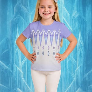 Puede incluir: Una ni&ntilde;a peque&ntilde;a con una camiseta de color p&uacute;rpura claro con un dise&ntilde;o geom&eacute;trico en blanco, azul claro y p&uacute;rpura. La camiseta tiene cuello redondo y mangas cortas. Tambi&eacute;n lleva leggings blancos. El fondo es un dise&ntilde;o azul helado.